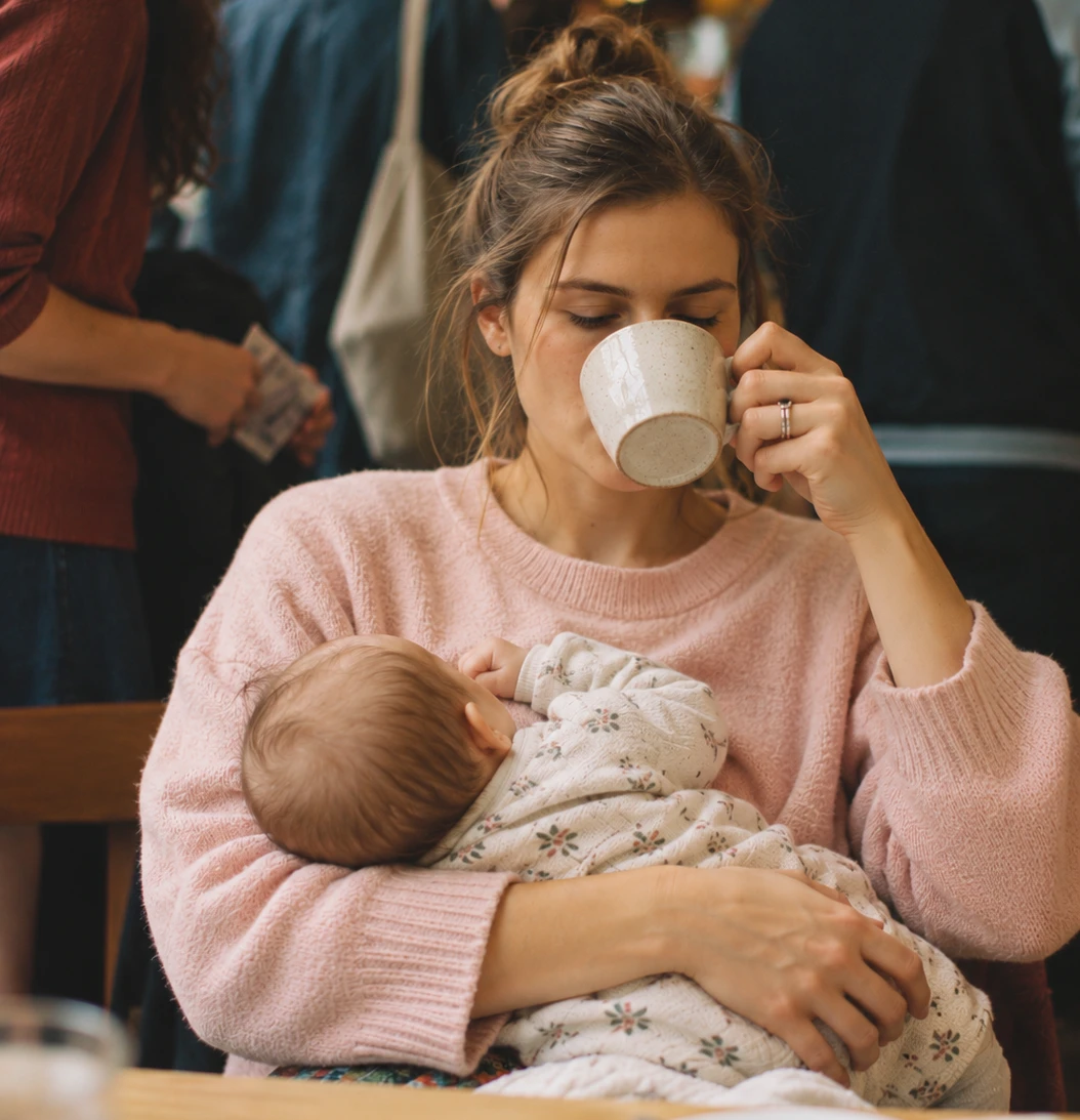 Mama geria kavą laikydama kūdikį ant rankų
